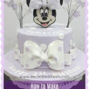 A single tier round purple cake with white polka dots, a Minnie Mouse face topper and butterflies and flowers side toppers. The cake has a large white bow on the front.
