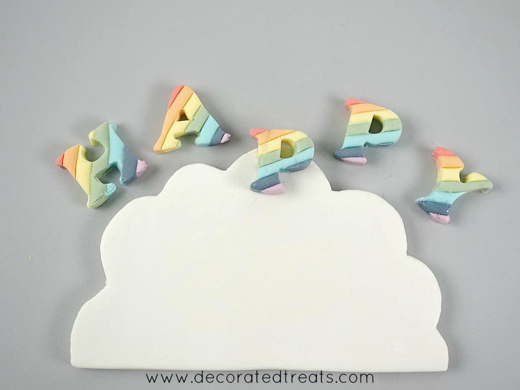A rainbow colored letter P on a white fondant cloud. On the sides is the letters H, A, P and Y