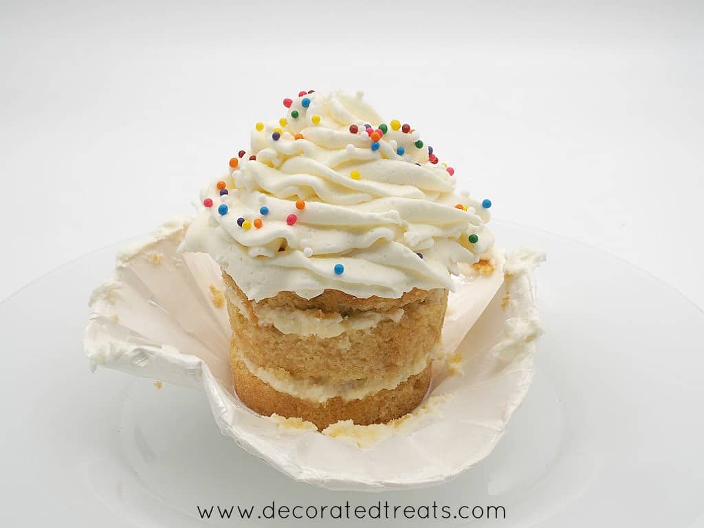A cupcake with its casing peeled off, and topped with buttercream and sprinkles
