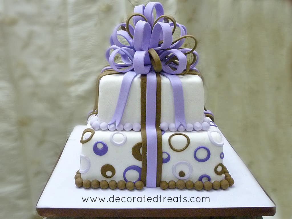 A two tier gift box cake decorated in brown and purple circle cut outs and pretty loop bow