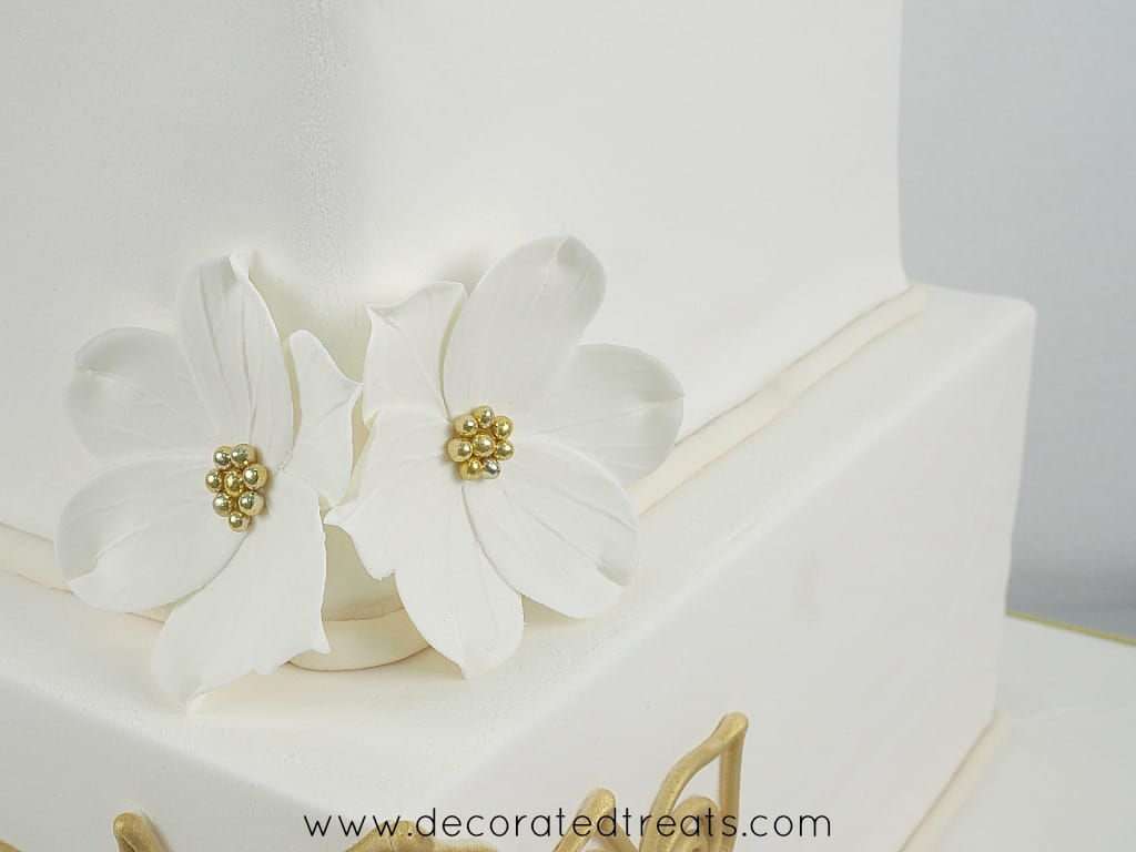 2 gum paste flowers with gold bead centers on the corner of a square cake