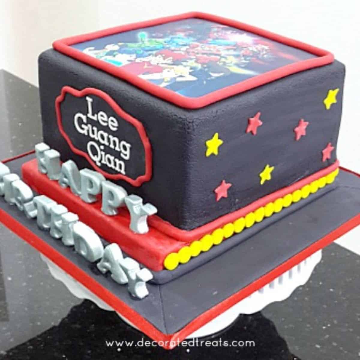 A black square cake with the Tenkai Knights edible image on top. Cake is decorated with red and yellow stars and the Happy Birthday alphabets in silver 3D
