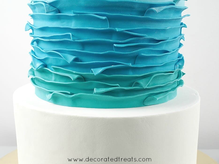 Second tier of a cake covered in blue and turquoise fondant strips