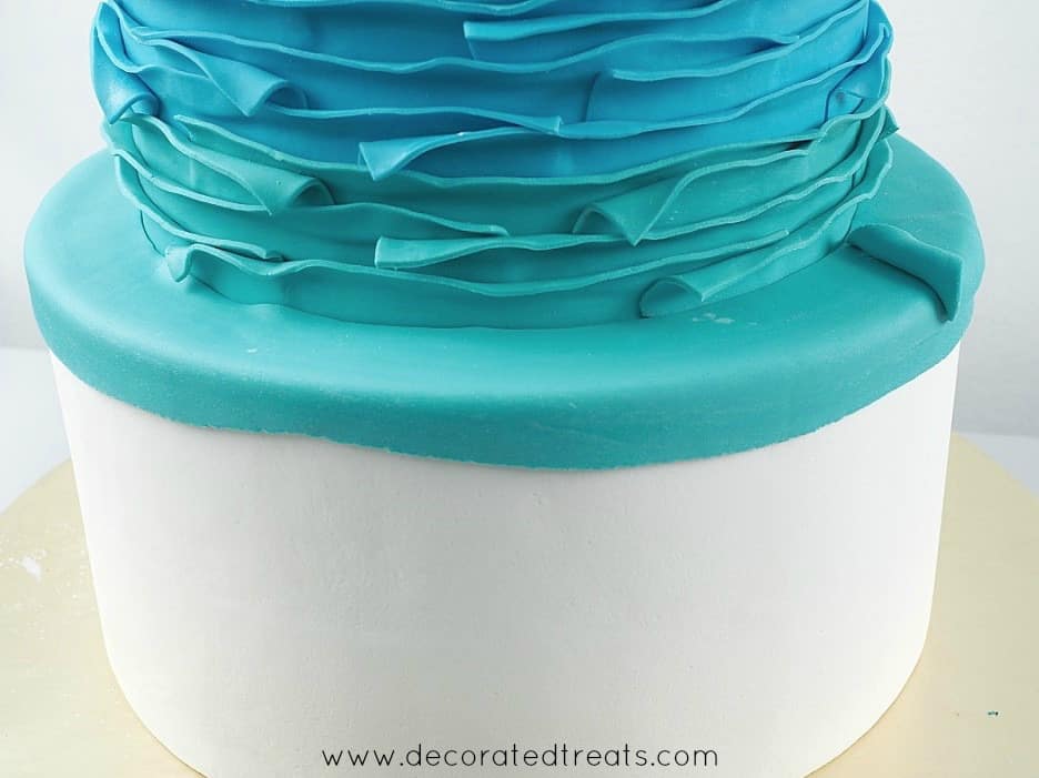 Second tier of a cake covered in blue and turquoise fondant strips