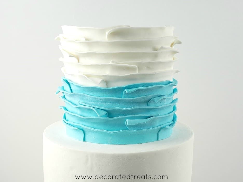 Top tier of a cake covered in white and blue fondant strips