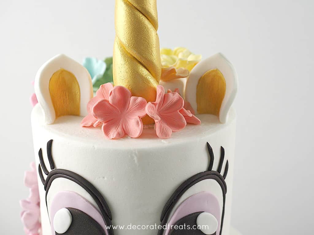 Top of a unicorn cake with gold horn and ears and simple colorful blossoms