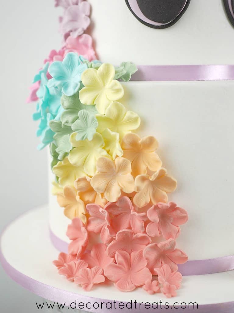 Cascading fondant flowers in colors of the rainbow on the sides of a 2 tier unicorn cake