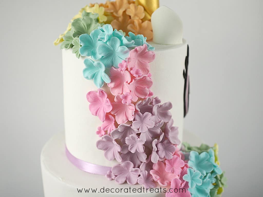 Cascading fondant flowers in colors of the rainbow on the sides of a 2 tier unicorn cake