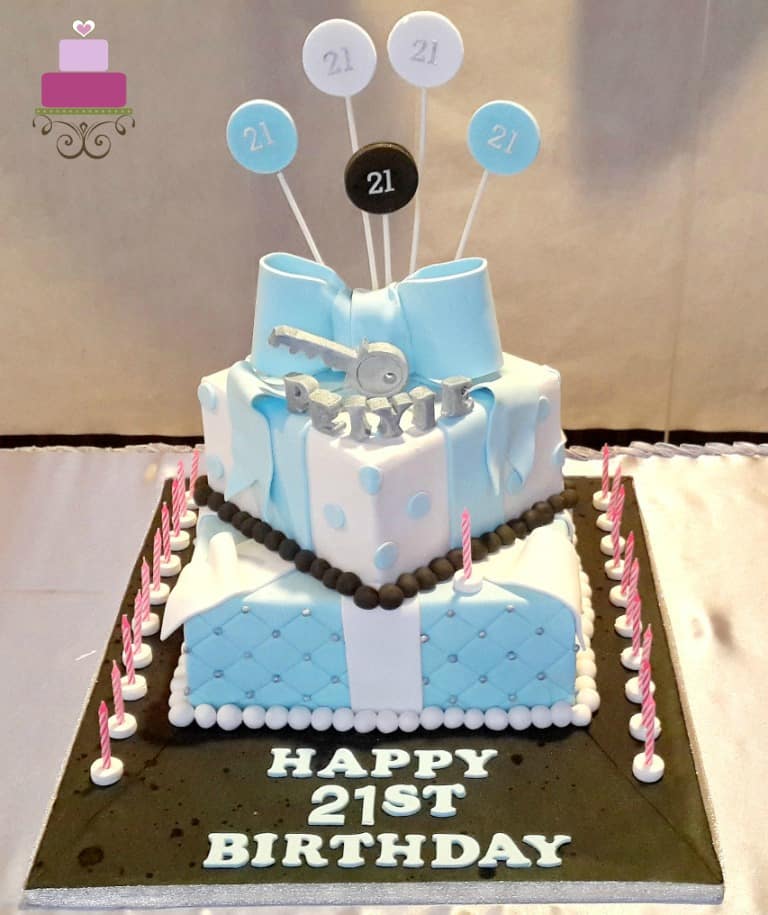 A 2 tier square birthday cake with a large blue bow and silver key topper