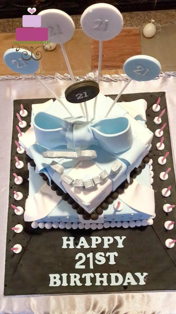 A 2 tier square birthday cake with a large blue bow and silver key topper