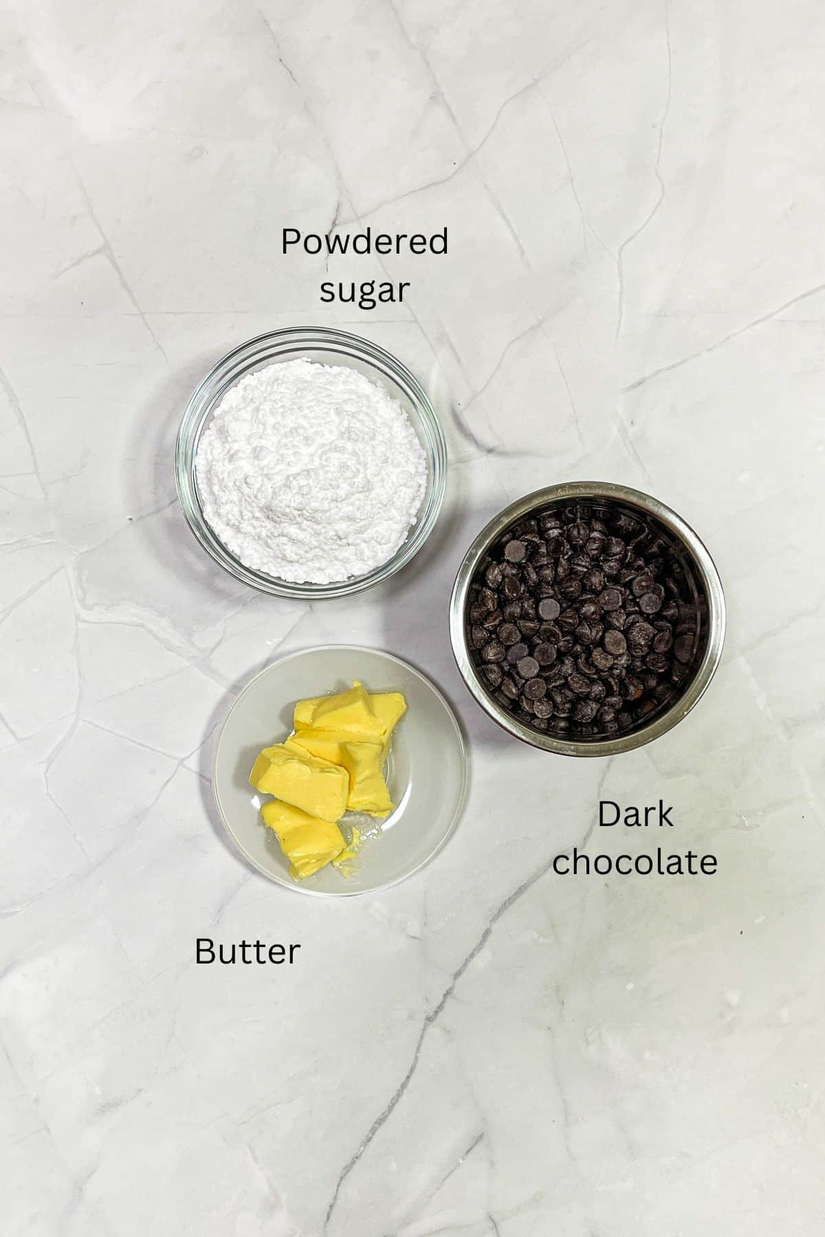 A bowl of powdered sugar, butter and chocolate chips against marble background.