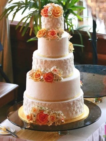 A5 tier wedding cake decorated with orange and yellow roses and fondant lace
