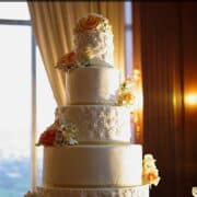 A 5 tier wedding cake decorated with orange and yellow roses and fondant lace