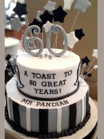 2 tier cake decorated in silver, black and white with a large number 60 topper and matching stars.