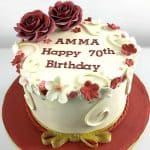 A round cake decorated with maroon and white fondant flowers and 2 large maroon roses.