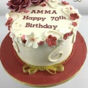 A round cake decorated with maroon and white fondant flowers and 2 large maroon roses.