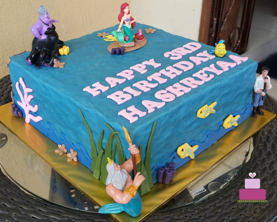 A square blue cake decorated with Ariel the Little Mermaid characters.