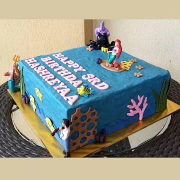 A square blue cake decorated with Ariel the Little Mermaid characters