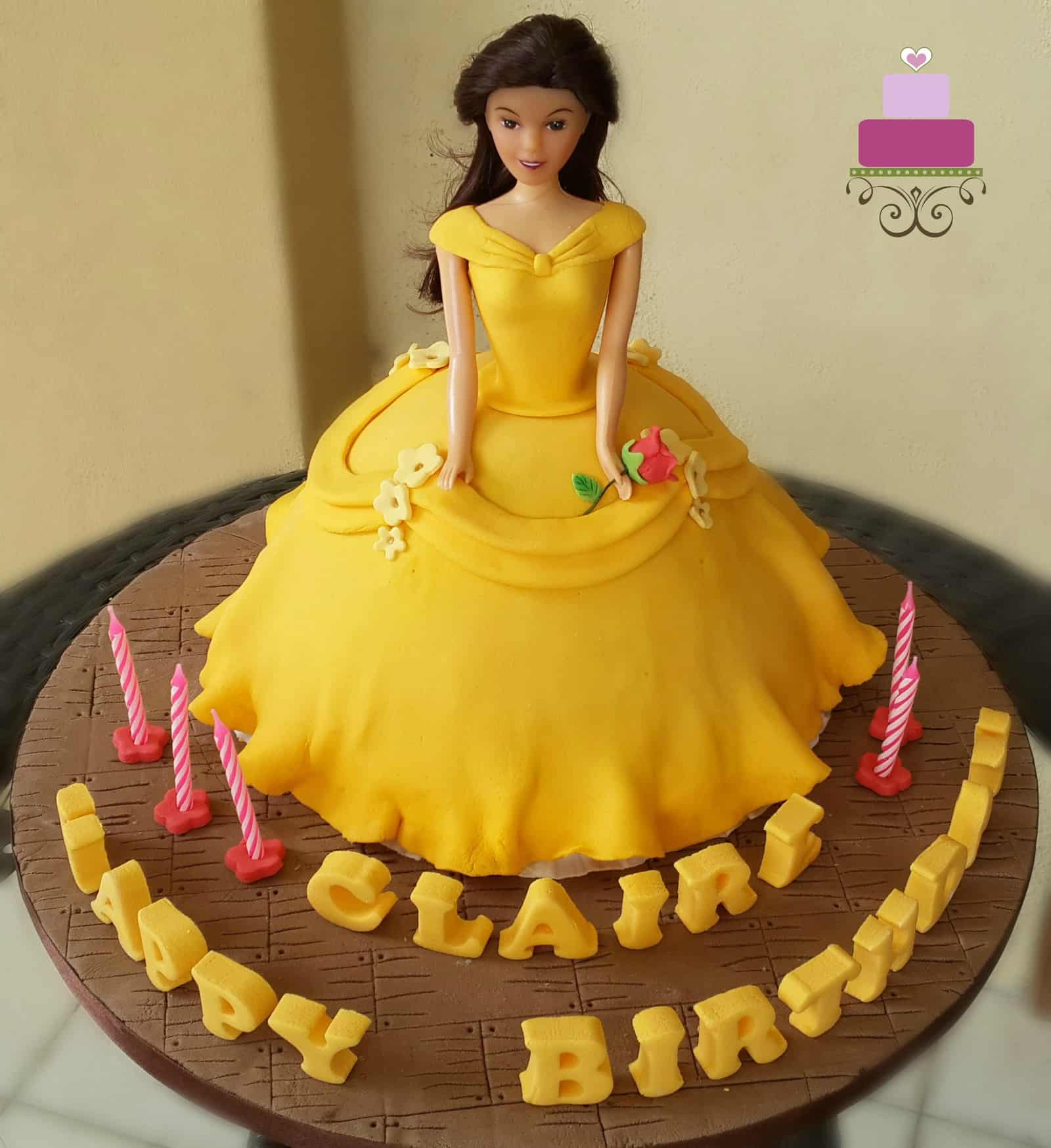 A doll cake decorated in yellow gown and a stalk of rose