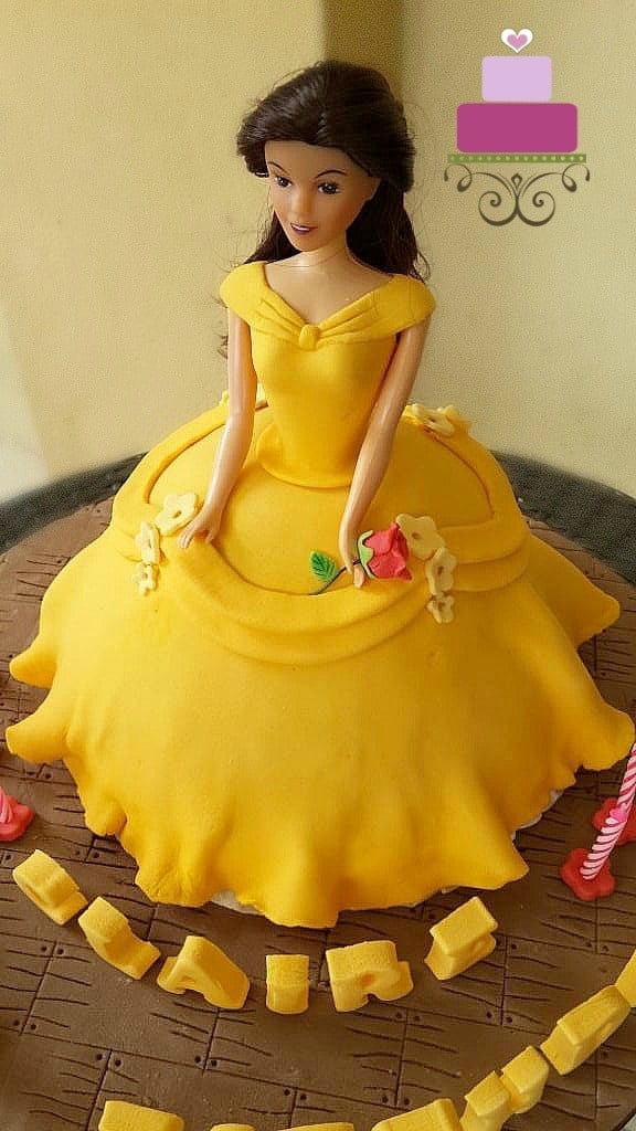 A princess cake decorated in yellow gown and a stalk of rose 