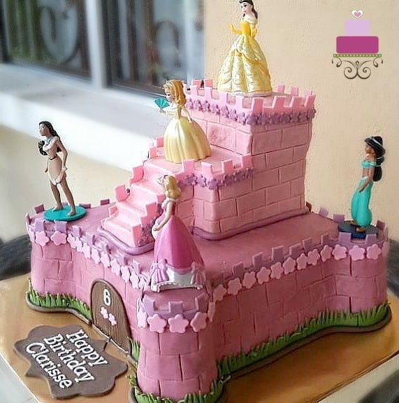A two tier castle cake in pink, decorated with 6 Disney princess toy toppers