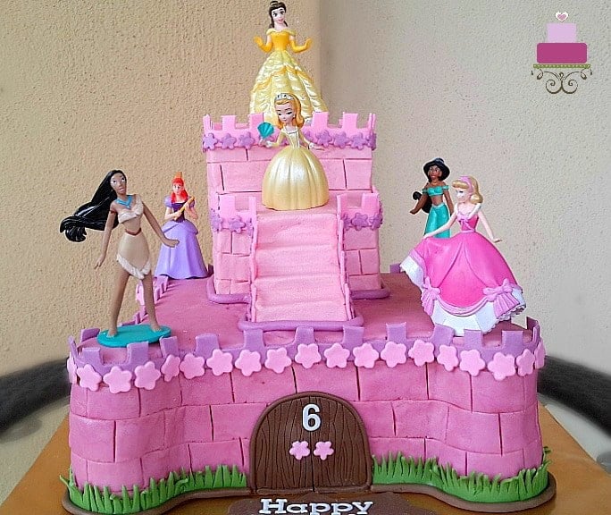 A two tier castle cake in pink, decorated with 6 Disney princess toy toppers