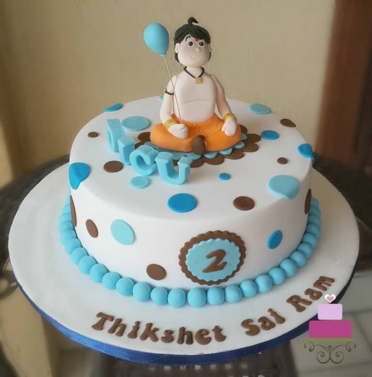 A round cake with blue and brown polka dots and Chhota Bheem cake topper holding a blue balloon.