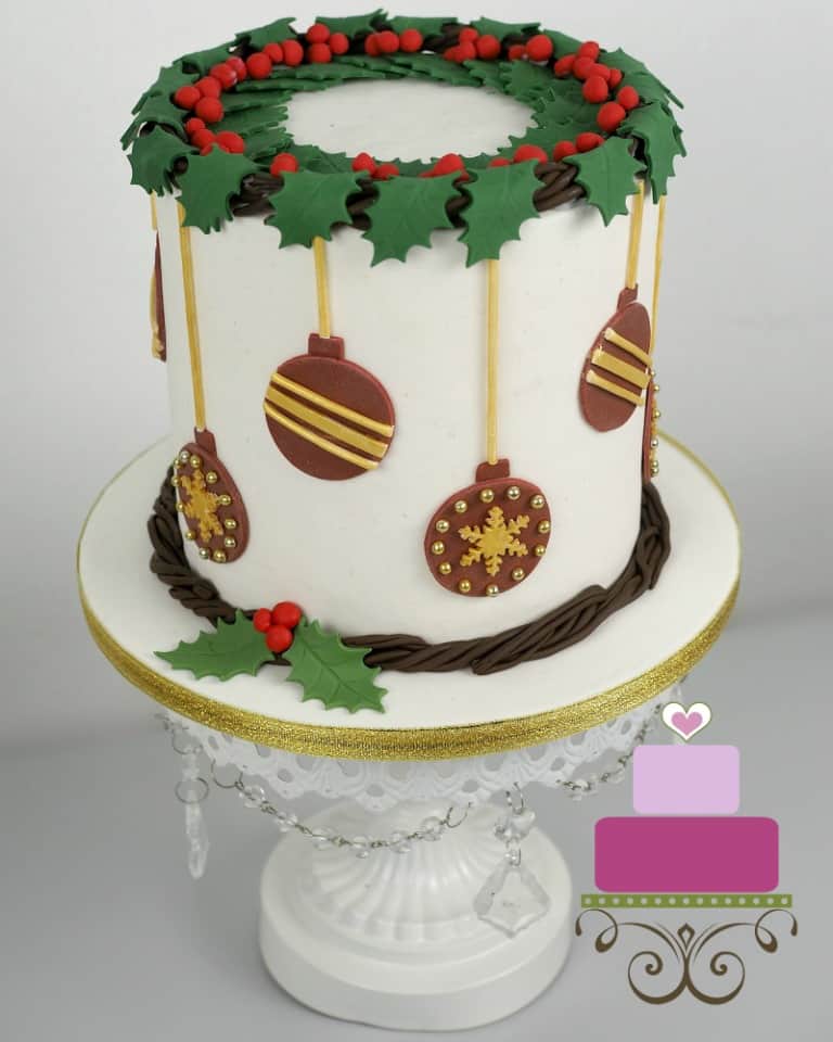A round cake decorated with holly garland and fondant baubles.