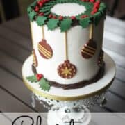 A round cake decorated with holly garland and fondant baubles.