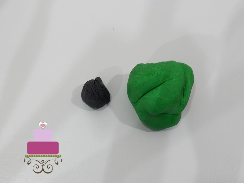 A small lump of black fondant next to a large lump of green fondant