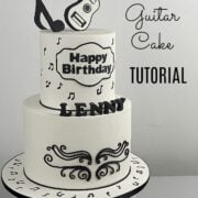 A black and white 2 tier cake with guitar topper and black music note topper.