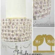 A 2 tier cake with the second tier covered in purple hydrangeas. Cake topper is a gold Mr & Mrs Birds paper pick.