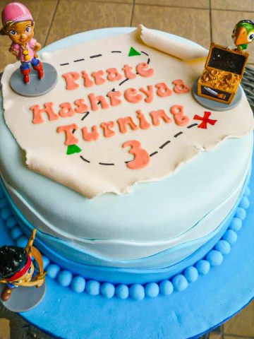 A round cake with a fondant pirate map and Jake and the Neverland Pirates toy toppers.