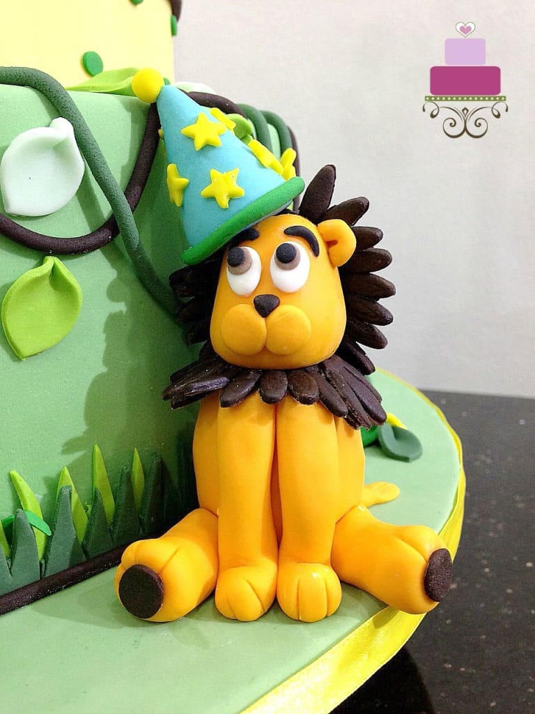3D fondant lion wearing a party hat, sitting on a cake board