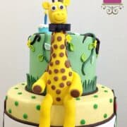 3D fondant giraffe with a bow, sitting on a cake.