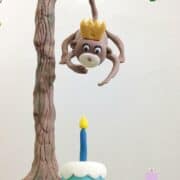A fondant monkey hanging down a fondant tree on a cake.