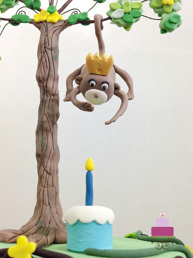 A fondant monkey hanging down a fondant tree on a cake.