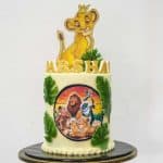 A round double barrel cake decorated with Simba cake topper, Lion King edible image and green fondant palm leaves.