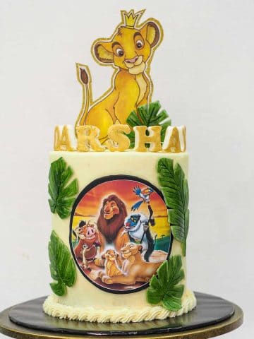 A round double barrel cake decorated with Simba cake topper, Lion King edible image and green fondant palm leaves