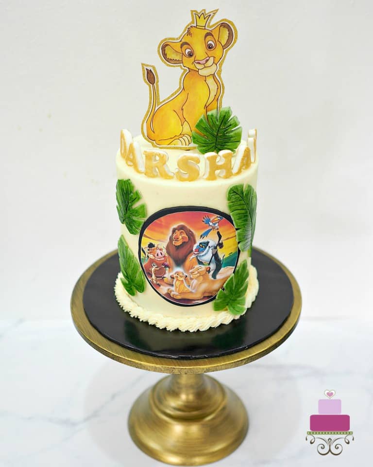 A round double barrel cake decorated with Simba cake topper, Lion King edible image and green fondant palm leaves