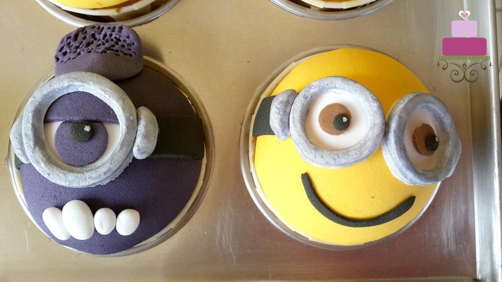 2 cupcakes decorated with yellow and purple minion faces.