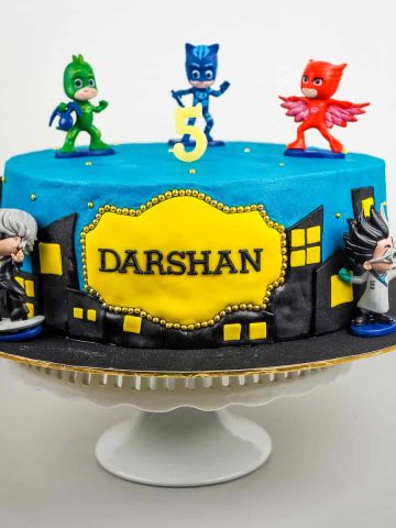 A round cake in blue with PJ Masks characters cake toppers.