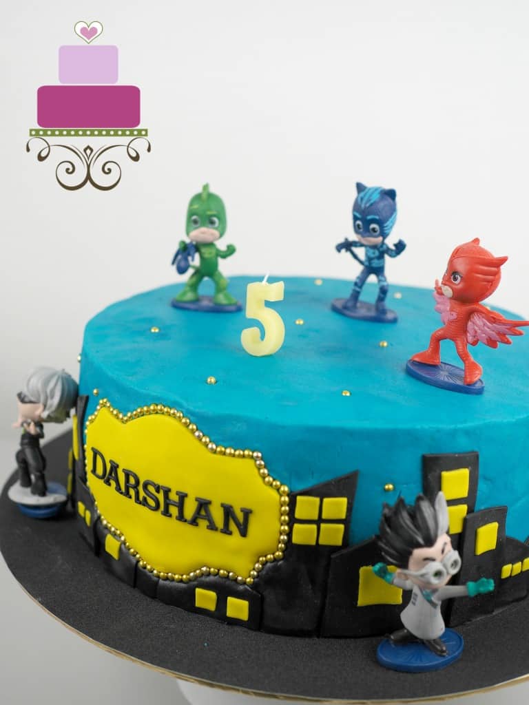 A round cake in blue with PJ Masks characters cake toppers