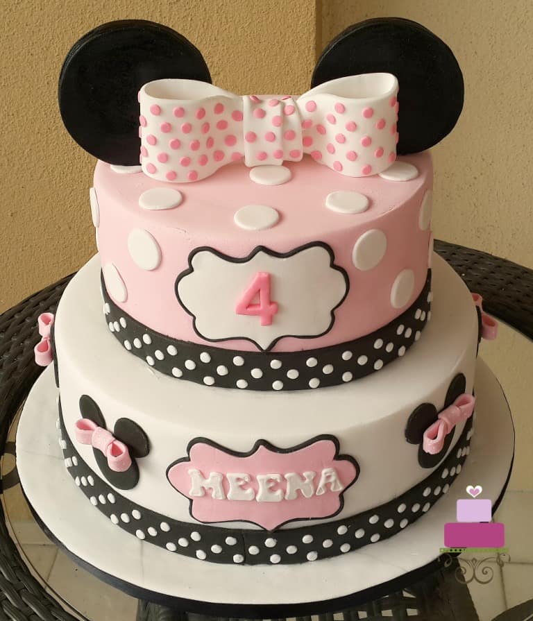 A 2 tier pink Minnie Mouse themed birthday cake with a large pink polka dots topper.