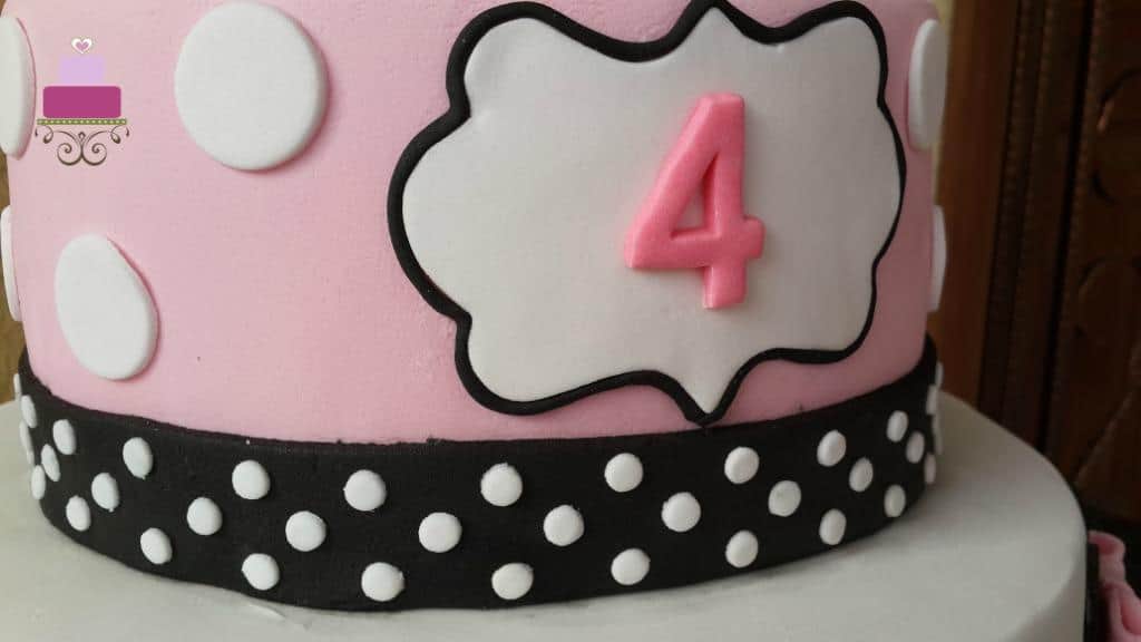 Number 4 on a white fondant plaque on a pink cake.