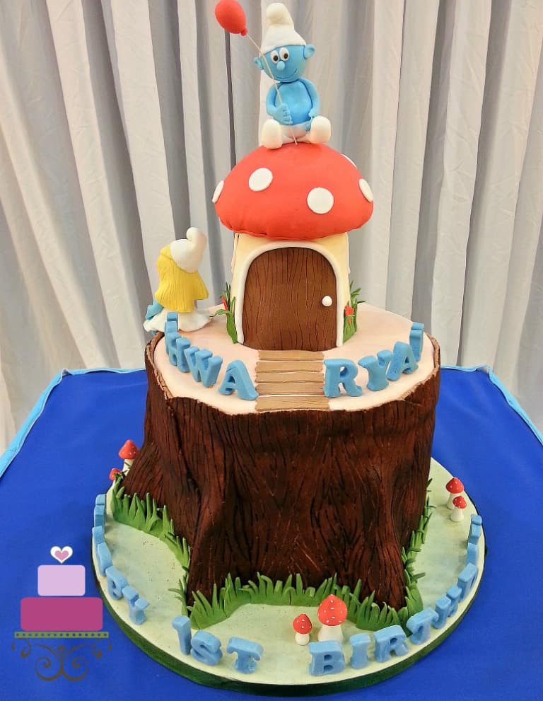 A mushroom on a tree stump cake decorated in Smurfs theme. A 3D Smurf in fondant is the cake topper.