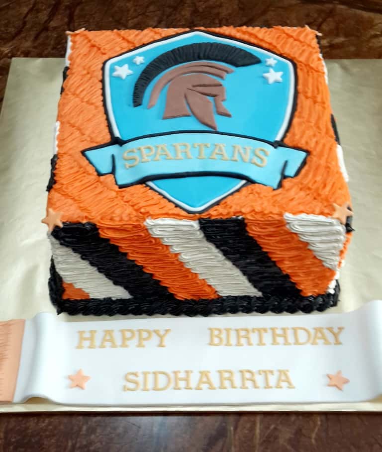 A square cake with orange, black and white side strips and a Spartans logo