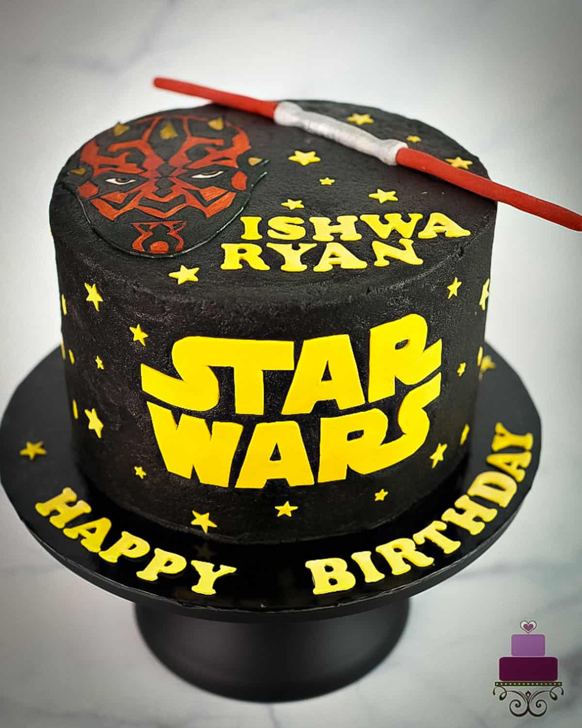 A round cake with black buttercream, Star Wars logo and Darth Maul and lightsaber topper.