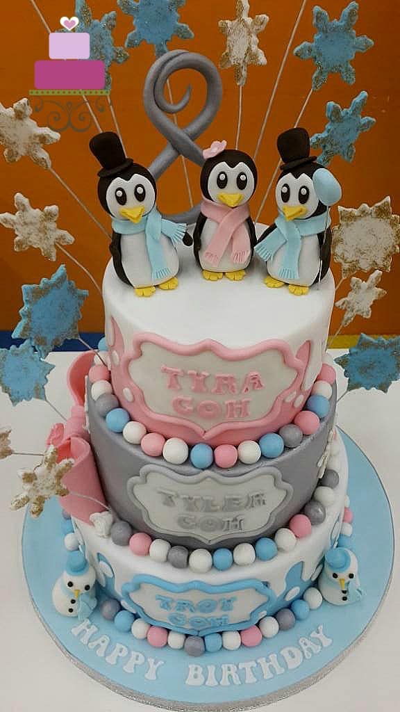 A 3 tier cake in blue, silver and pink and 3 cute penguins toppers.