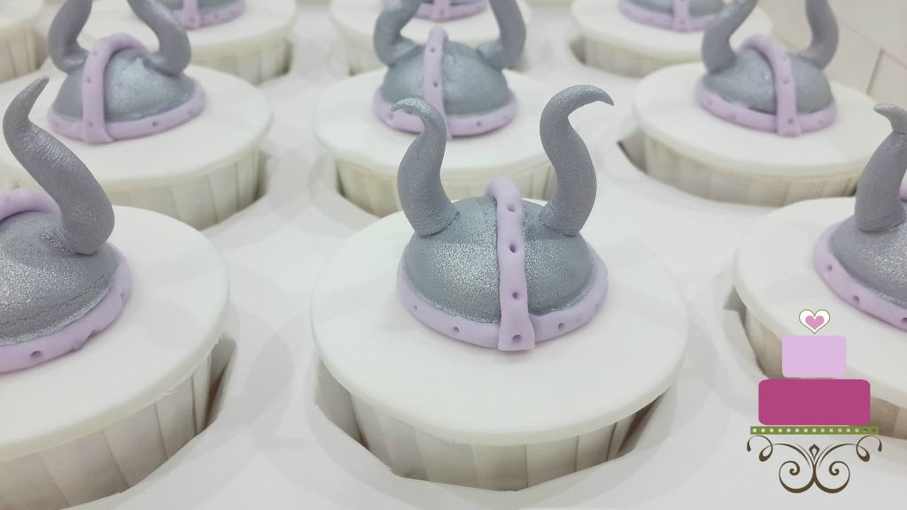 White cupcakes with fondant viking helmet toppers in silver and purple